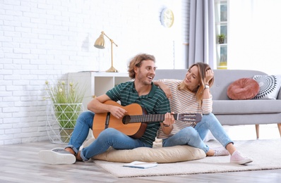 Young man playing acoustic guitar for his girlfriend in living room