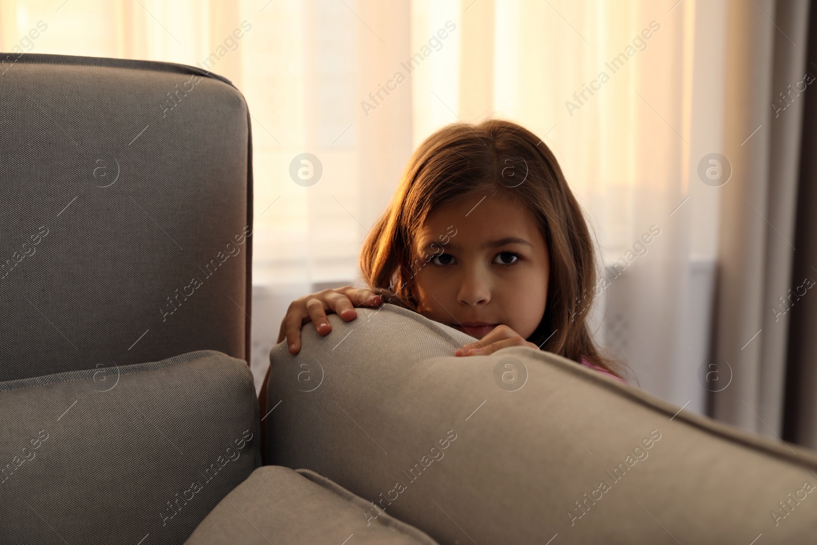 Photo of Sad little girl hiding behind sofa at home. Domestic violence concept