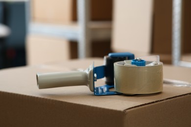 Photo of Adhesive tape dispenser on cardboard box indoors