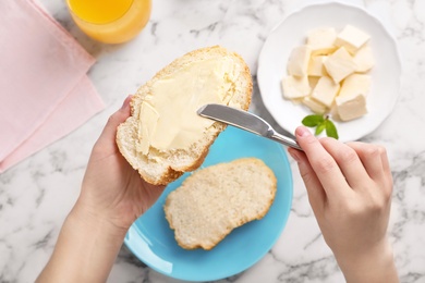 Photo of Woman spreading butter on slice of bread over table, closeup