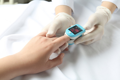Doctor examining patient with fingertip pulse oximeter in bed, closeup