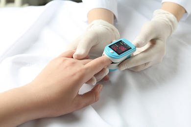 Photo of Doctor examining patient with fingertip pulse oximeter in bed, closeup