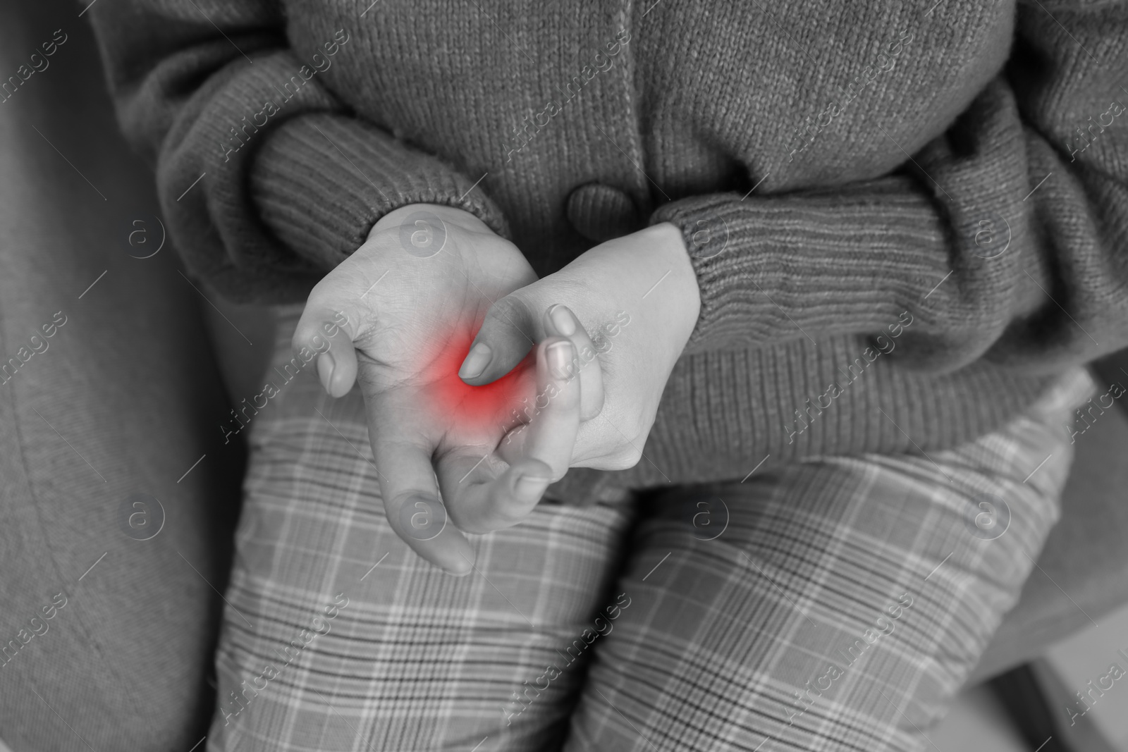 Image of Woman suffering from trigger finger on armchair, closeup. Black and white photo with red accent