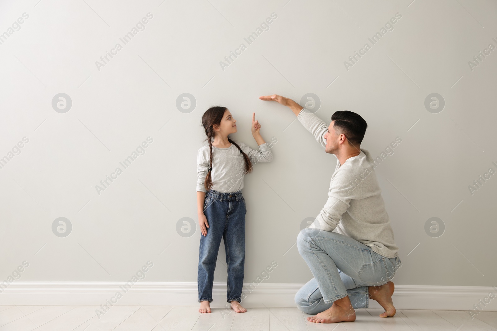 Photo of Father measuring little girl's height near light grey wall indoors