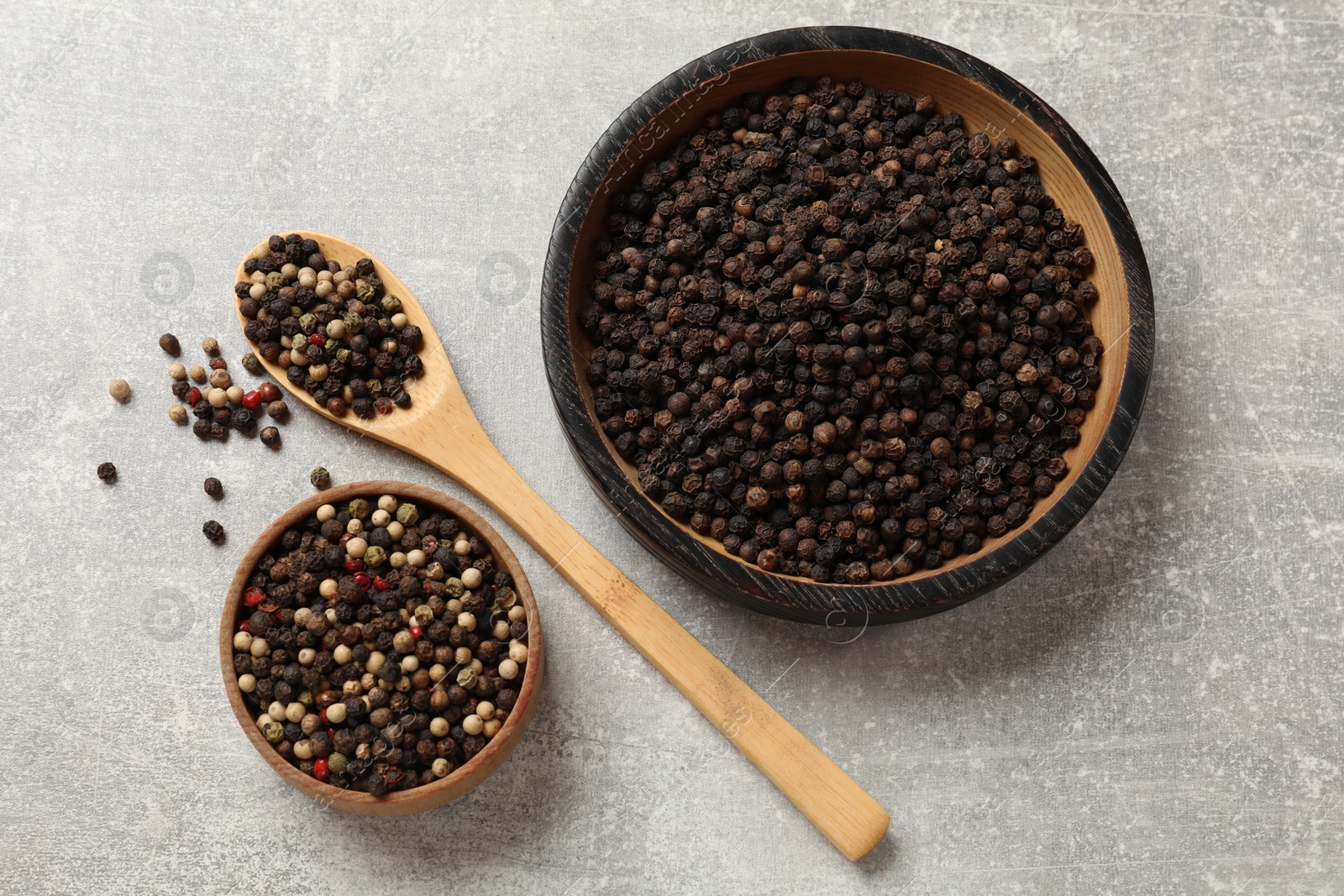 Photo of Aromatic spice. Different peppers in bowls and spoon on grey table, flat lay