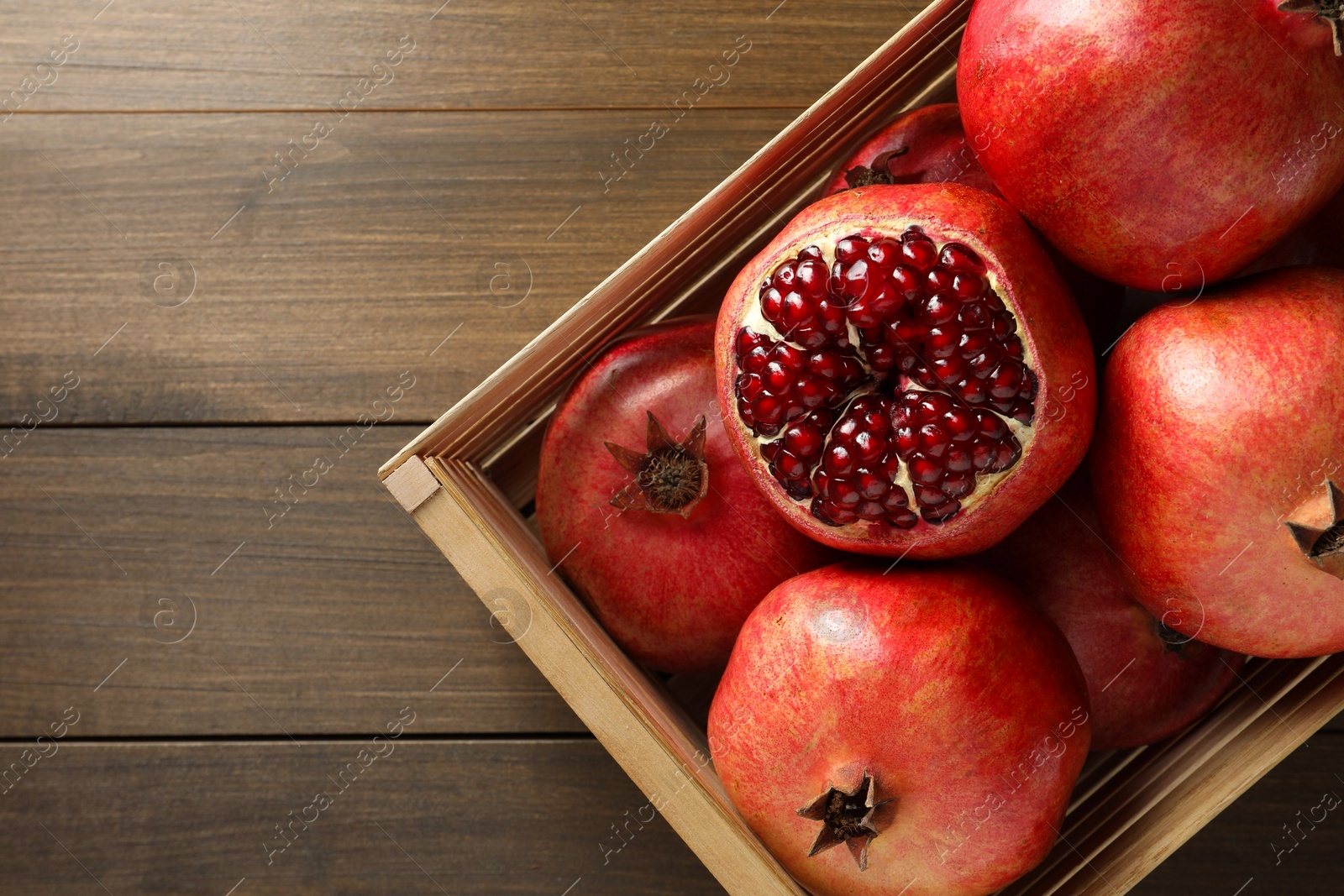 Photo of Ripe pomegranates in crate on wooden table, top view. Space for text