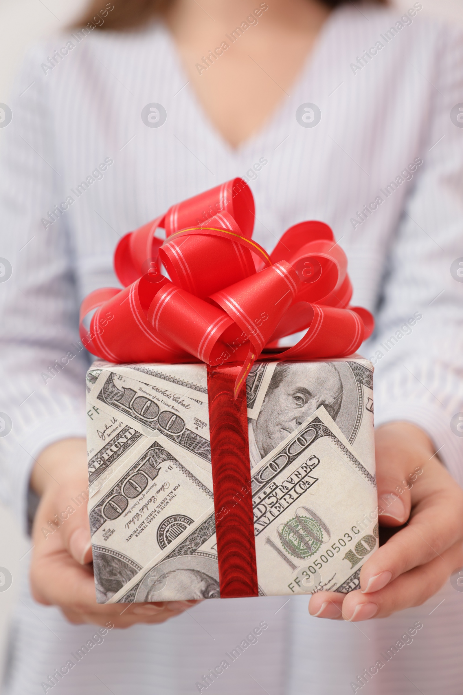 Photo of Woman holding gift box wrapped in dollars, closeup