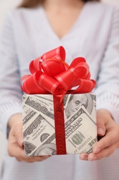 Photo of Woman holding gift box wrapped in dollars, closeup