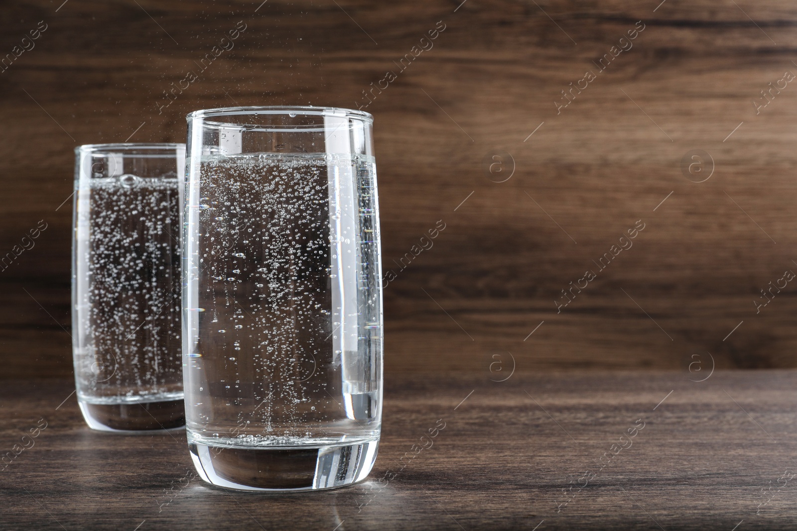 Photo of Glasses of soda water on wooden table. Space for text