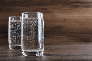 Photo of Glasses of soda water on wooden table. Space for text
