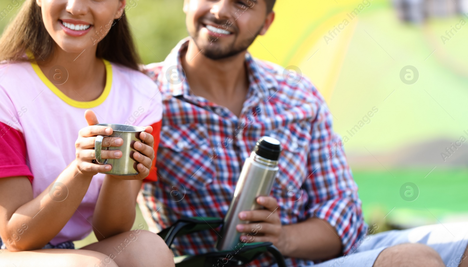 Photo of Young couple with hot drinks resting outdoors, closeup. Camping vacation