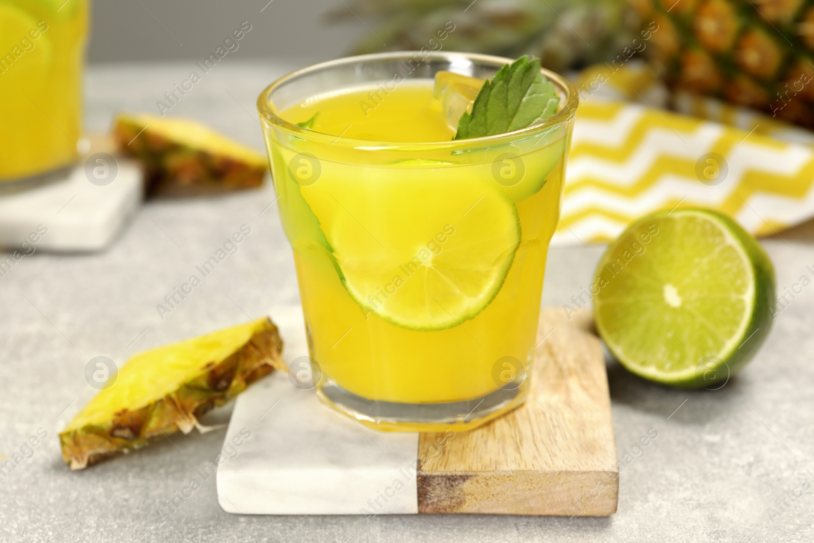 Photo of Glass of tasty pineapple cocktail with mint and lime on light grey table