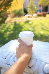 Woman with cardboard cup of coffee on stone bench outdoors, closeup