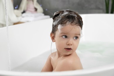 Photo of Cute little girl washing hair with shampoo in bathroom