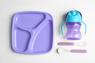 Set of plastic dishware on white wooden table, flat lay. Serving baby food