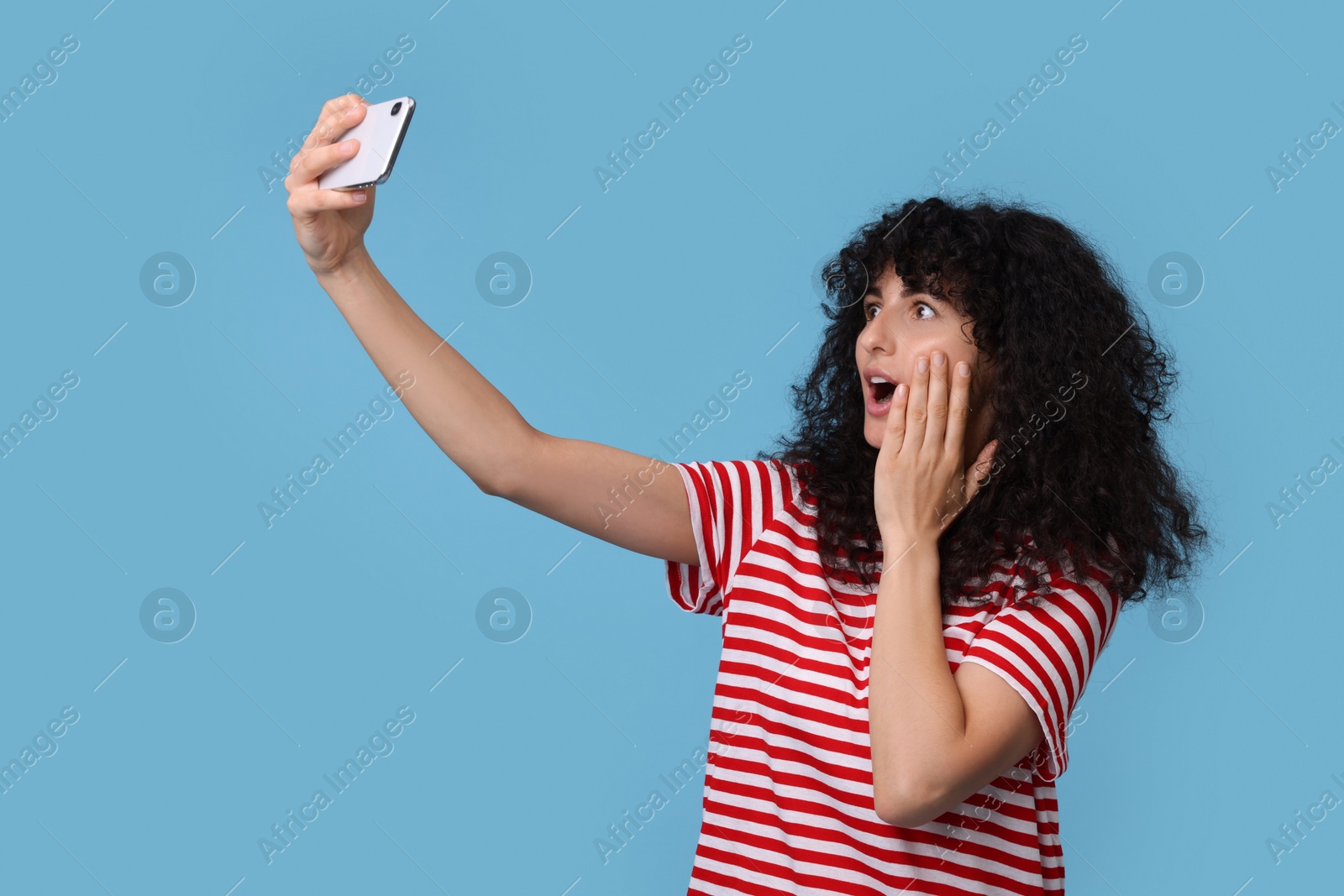 Photo of Emotional young woman taking selfie on light blue background