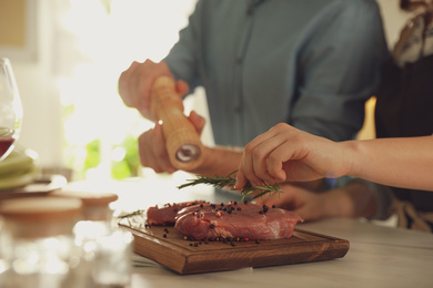 Photo of Lovely young couple cooking meat together in kitchen, closeup