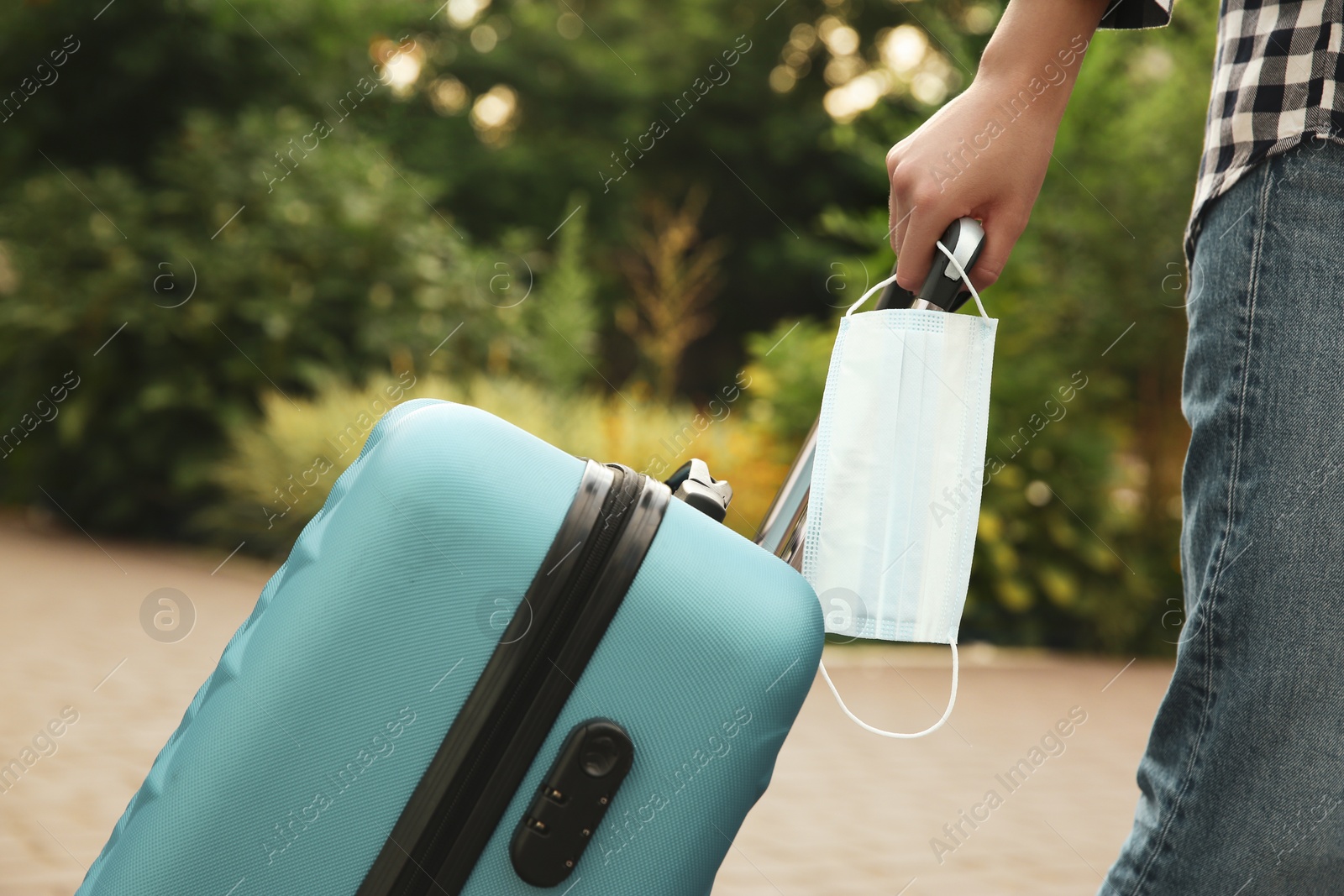 Photo of Woman with suitcase and protective mask outdoors, closeup. Travelling during coronavirus pandemic