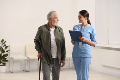 Photo of Smiling nurse with clipboard talking to elderly patient in hospital