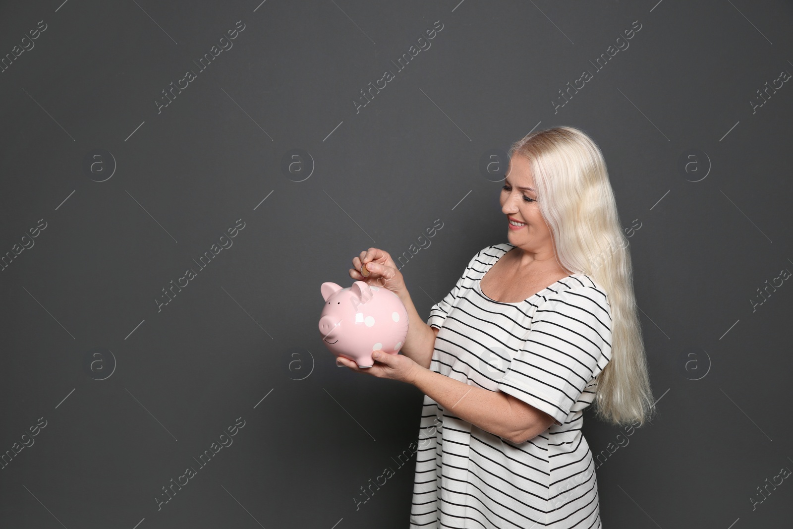 Photo of Mature woman putting money into piggy bank on grey background. Space for text