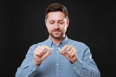 Photo of Stop smoking concept. Man holding pieces of broken cigarette on black background