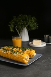 Photo of Delicious boiled corn cobs with butter and parsley on gray table against black background