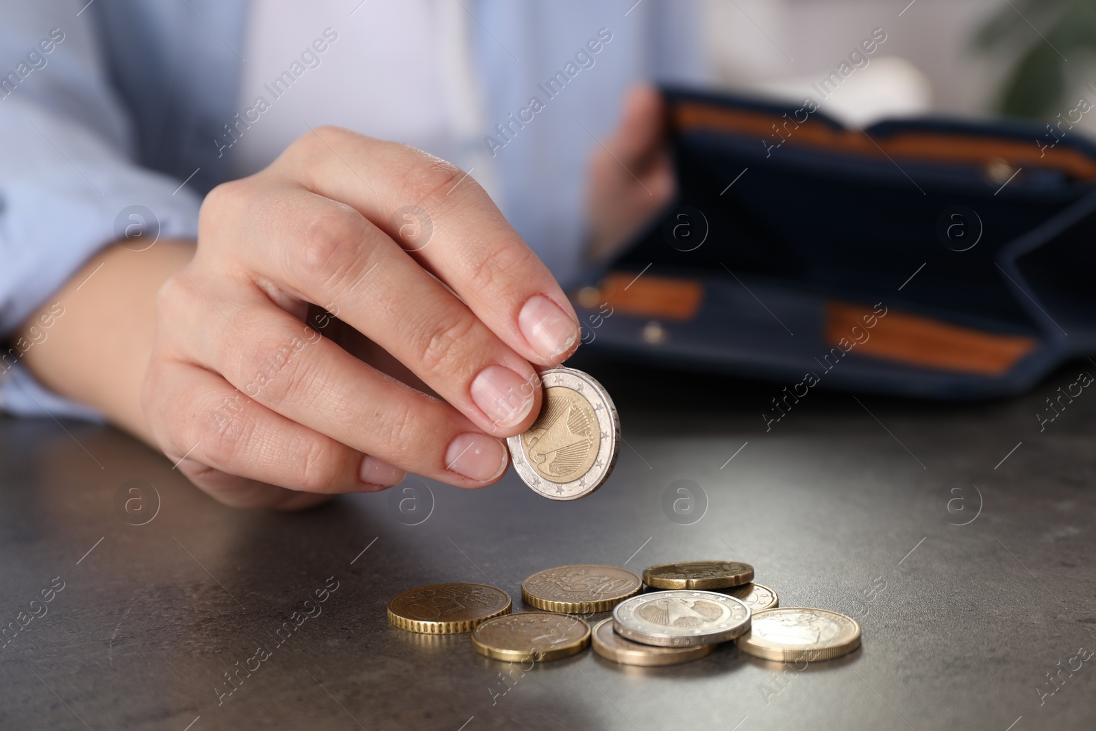 Photo of Poor woman counting coins at grey table indoors, closeup