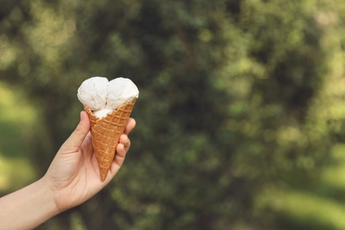 Photo of Woman holding delicious ice cream in waffle cone outdoors, closeup of hand. Space for text