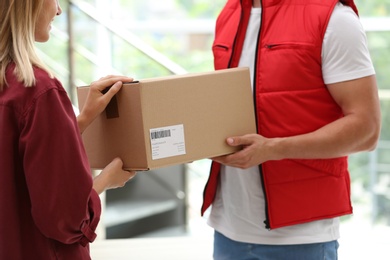 Photo of Woman receiving parcel from delivery service courier indoors