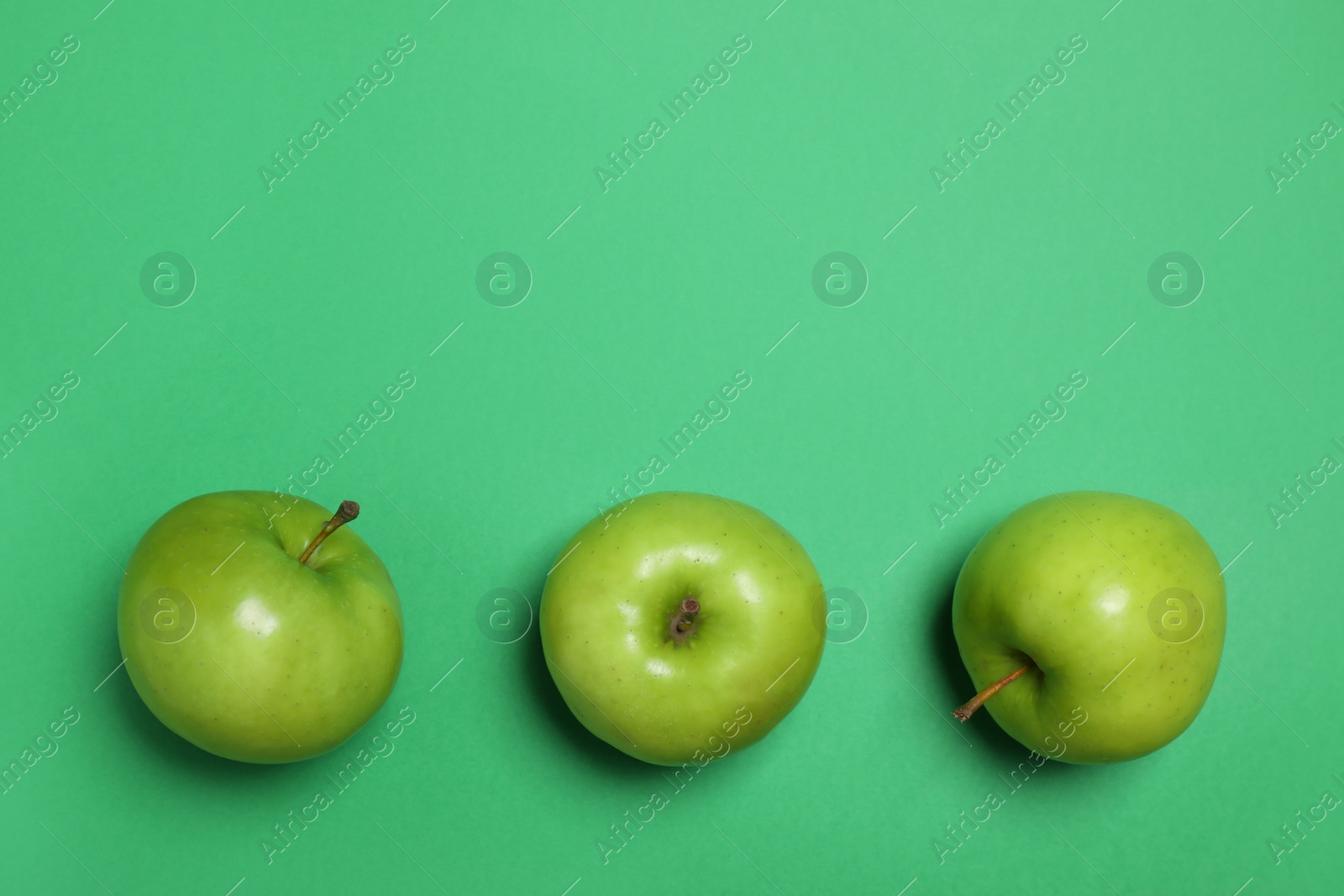 Photo of Apples on green background, flat lay. Space for text
