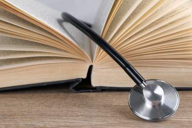 Open student textbook and stethoscope on wooden table, closeup. Medical education