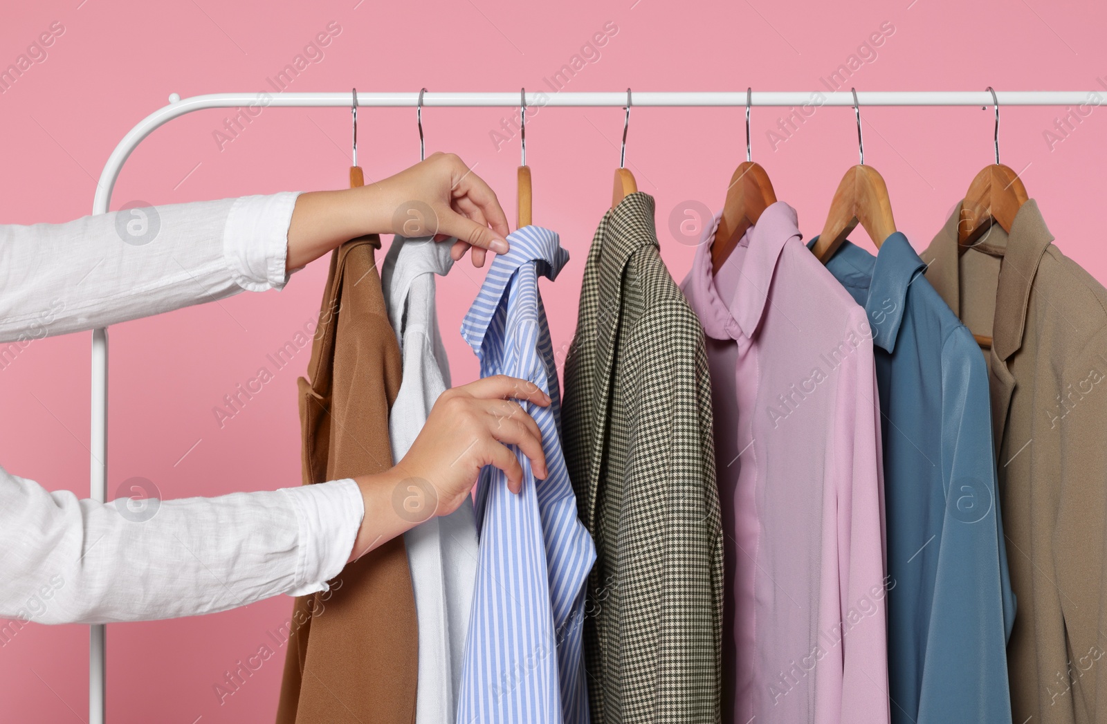 Photo of Woman taking stylish shirt from clothes rack against pink background, closeup