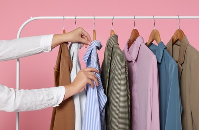 Woman taking stylish shirt from clothes rack against pink background, closeup