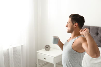 Man with cup of coffee in bedroom. Lazy morning