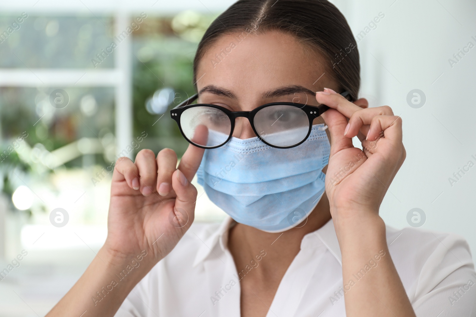 Photo of Woman wiping foggy glasses caused by wearing medical mask indoors, closeup