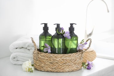 Photo of Wicker basket with soap dispensers , flowers and clean towels on table