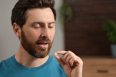 Photo of Handsome man taking pill indoors, space for text