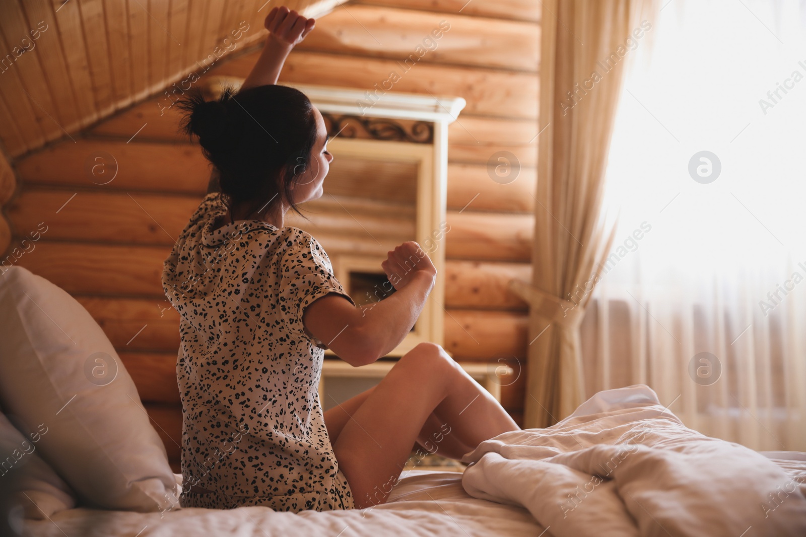 Photo of Young woman in pajamas stretching on bed at home. Lazy morning