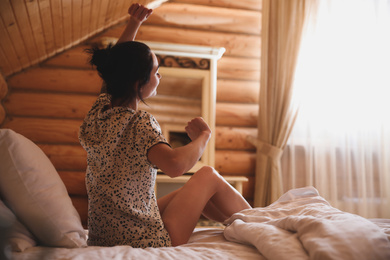 Photo of Young woman in pajamas stretching on bed at home. Lazy morning