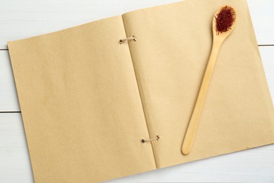 Photo of Blank recipe book and spoon with saffron on white wooden table, flat lay. Space for text