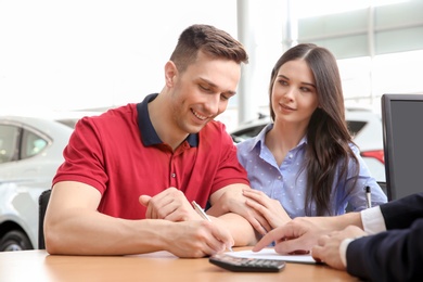 Photo of Young couple buying new car at dealership