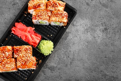 Photo of Tasty sushi rolls in box on grey table, top view with space for text. Food delivery