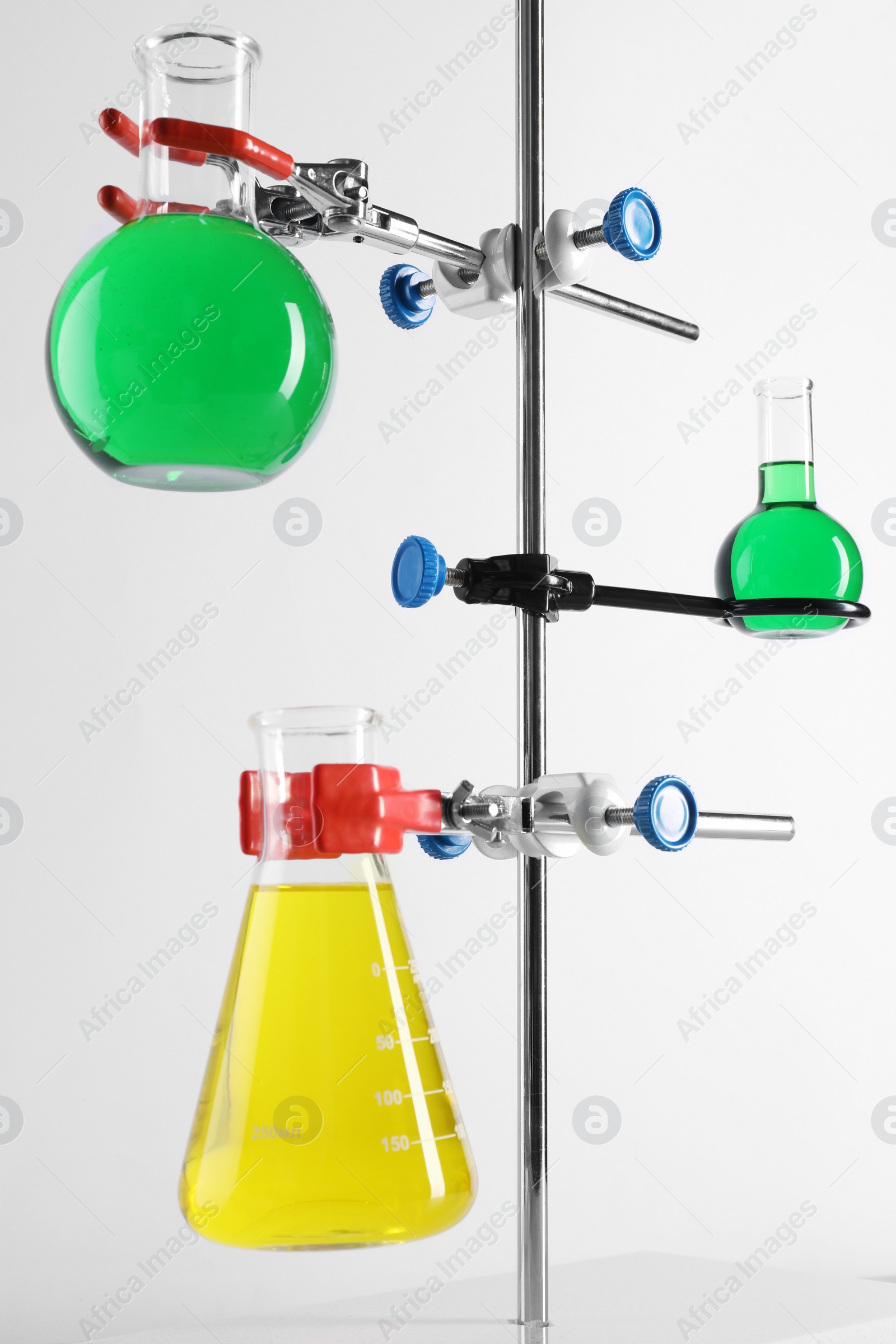 Photo of Retort stand and laboratory flasks with liquids on white background