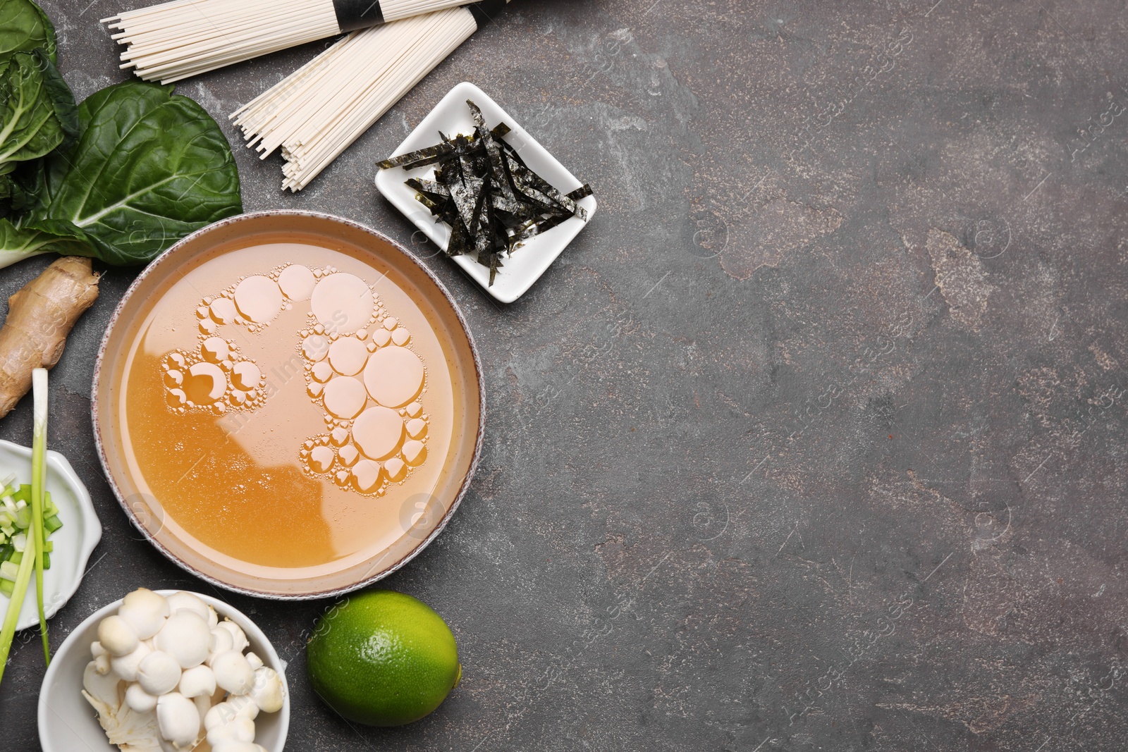 Photo of Cooking delicious ramen soup. Different ingredients on gray table, flat lay. Space for text