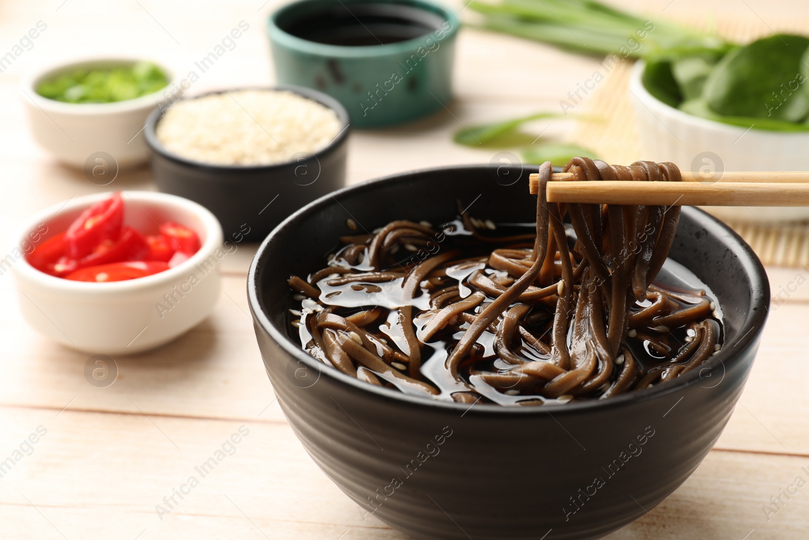 Photo of Eating delicious buckwheat noodle (soba) soup with chopsticks at white wooden table, closeup