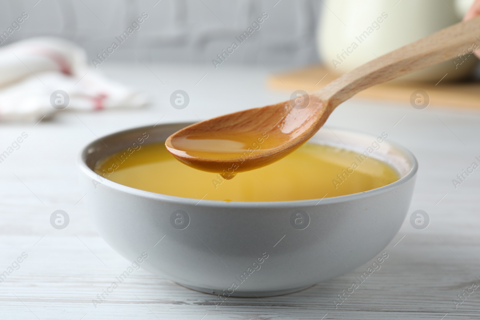 Photo of Spoon of clarified butter over bowl on white wooden table