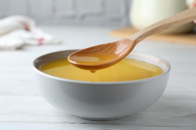 Spoon of clarified butter over bowl on white wooden table