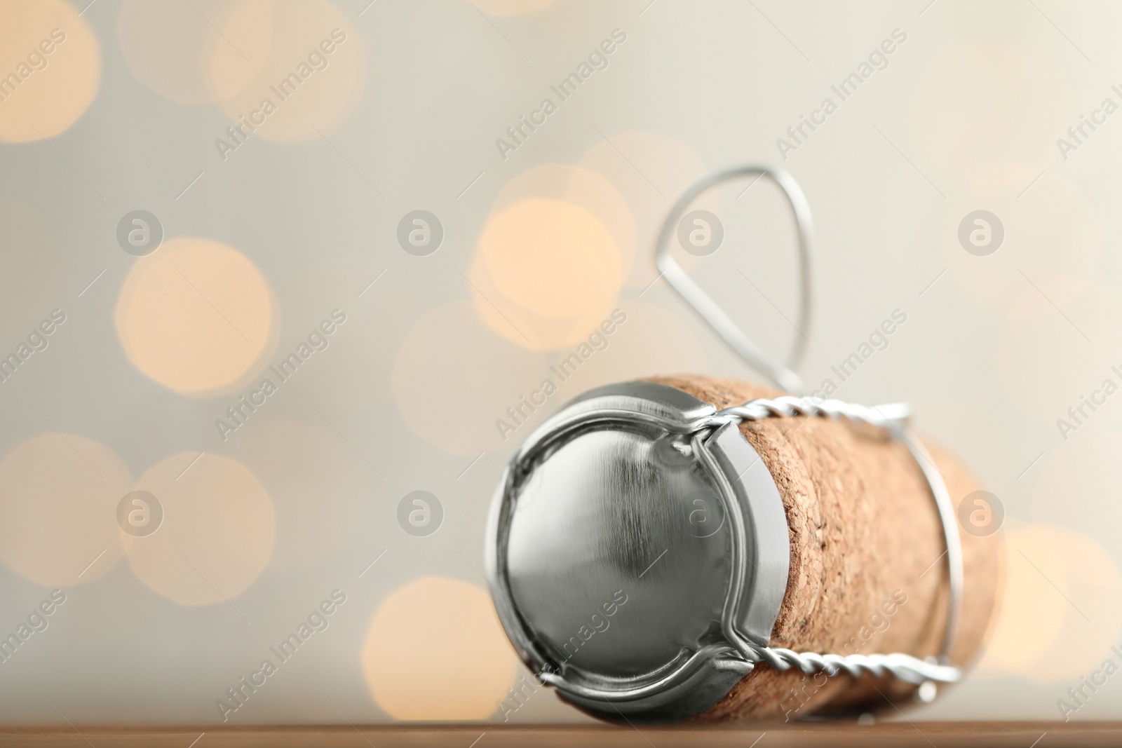 Photo of Sparkling wine cork with muselet cap on table against blurred festive lights, closeup. Space for text