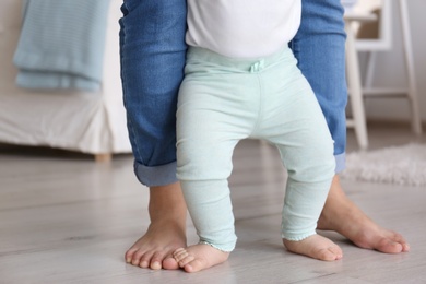 Photo of Baby doing first steps with mother's help, closeup of legs