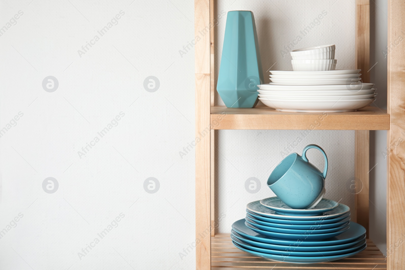 Photo of Shelving unit with set of dinnerware on light background, space for text. Interior element